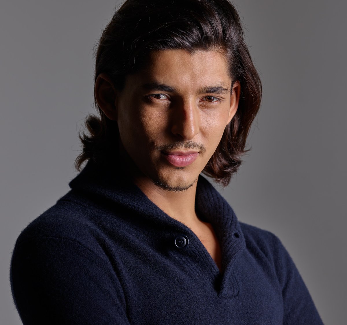 Professional headshot of a male artist with dark long hair wearing a blue sweater taken at NYC Headshot.